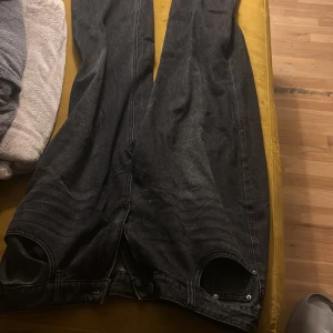 Svarta wide jeans med dragkedja - Säljer ett par svarta jeans med breda ben och coola dragkedjor vid bensluten. Jeansen har en mörk tvätt och klassisk femficksdesign. Perfekta för dig som gillar en avslappnad och trendig stil.