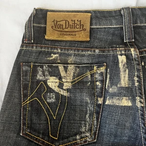 Von Dutch jeans - Mörkblå jeans från Von Dutch med coolt gult tryck och logga på bakfickorna samt över rumpan. Jeansen har slitna detaljer, kontrastsömmar och klassisk femficksdesign. Materialet är denim med en rak passform och låg midja. Byxorna är gamla och använda men har ingen större defekt som inte är med på bildera. Jeansen är rätt så små i modellen, passar min lillasyster som är 160cm som bär storlek xs/s oftast i jeans.🩷PRISET KAN DISKUTERAS!!💕💕