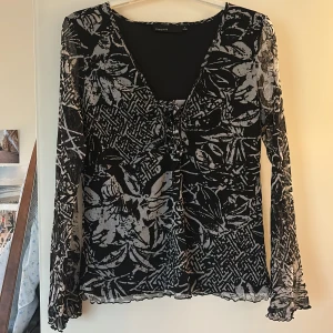 Svart blommig blus med snörning - Säljer en svart langärmad topp med super fin urringning och knytning. Tunn och lätt i materialet. Snygg och unik design som sticker ut. Nästintill oanvänd. Stär storlek L men passar ocksa M 🤍