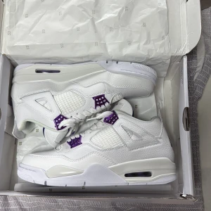 Nike Air Jordan 4 vit/lila sneakers - Nike Air Jordan 4 sneakers i vitt skinn med lila detaljer på snörningen och sulan. Klassisk meshpanel på sidorna, Jumpman-logga på plösen och undersidan. Snygg och sportig siluett med hög komfort och coola kontraster.