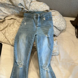 Ljusblå bootcut jeans med slits - Säljer ett par ljusblå jeans med bootcut-modell och slitningar på knäna. Jeansen har hög midja och slits nertill på benen för en trendig look. Perfekta för dig som gillar en avslappnad men ändå snygg stil.