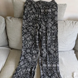 Svarta tunna byxor med resår - Svarta byxor från Lindex med vitt grafiskt mönster och bekväm resår i midjan. Mycket skönt och luftigt material. Sköna att ha en varm sommardag. 