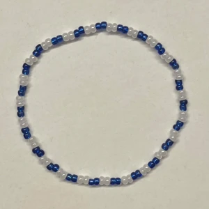 Blåvitt pärlarmband - Ett tunt armband med små blå och vita pärlor i ett enkelt och randigt mönster. Armbandet är elastiskt och kan göras i flera storlekar och färger. Jättegullig accessoar till en outfit💓