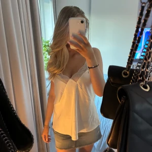 Vit spetsdetaljerad linnetopp Lindex - Säljer en vit linnetopp från Lindex med tunna axelband och v-ringning. Toppen har fina spetsdetaljer upptill och en lätt glansig finish. Perfekt för dig som gillar en feminin och stilren look.🐬🌟🌸