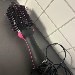 Revlon svart och rosa varmluftsborste - En svart och rosa varmluftsborste från Revlon med ovala borsthuvud och täta borst med rosa toppar. Perfekt för att styla och föna håret samtidigt. Ergonomiskt handtag och lång sladd för smidig användning.