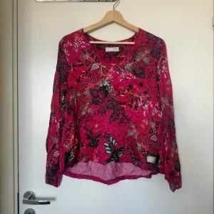 Odd Molly blommig blus i rosa - Färgstark blus i rosa med blommigt mönster och fjärilar. Långärmad modell med v-ringning och avslappnad passform. Tunn och luftig, perfekt för vår och sommar. Snygga detaljer i flera färger som gör den unik och lekfull. Från märket Odd Molly i storlek 1 som ungefär motsvarar en storlek S. Mycket fint skick, jag hittar inga synlig anmärkningar eller defekter.  