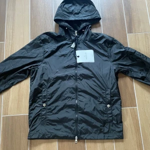 Ny Moncler Vattentät Vindjacka   - Moncler Vindjacka i nyskick - aldrig använd. Storlek M men kan passa S. Väldigt clean och sällsynt modell. Den är gjord av vattentåligt och väldigt skönt material samt sitter sjukt bra på kroppen. Passar alla outfits och matchar med alla färger. Kan frakta samt mötas upp!