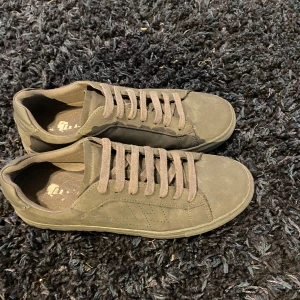 Grå sneakers i mocka-look - Snygga grå sneakers från Talin med klassisk design och platt sula. Skorna har rund tå, snörning och är gjorda i ett material som liknar mocka. Perfekta för dig som gillar stilrena och enkla sneakers till vardags.