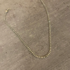Glittrigt silverfärgat halsband - Ett snyggt halsband i silverfärg med två rader gnistrande stenar som ger en riktigt glittrig look. Kedjan är tät och smidig, perfekt för att ge extra bling till din outfit. Lås i ena änden för enkel användning.
