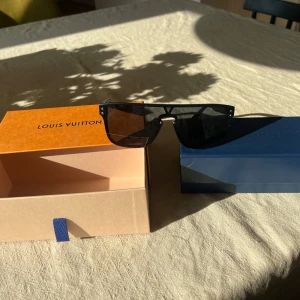 Louis Vuitton solglasögon  - Snygga svarta solglasögon från Louis Vuitton med monogrammönster på glasen. Modellen har en modern, kantig form och diskret logga på bågen. Kommer med originalbox och fodral. Perfekta för dig som vill sticka ut med lyxig streetstyle. Kvitto från inköp 2022