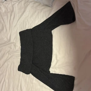 Mörkgrå offshoulder stickad tröja - Säljer en mörkgrå stickad tröja med offshoulder-modell och vida ärmar. Tröjan är ribbad och har en croppad passform som ger en trendig look. Perfekt för dig som gillar att sticka ut lite extra med din outfit.