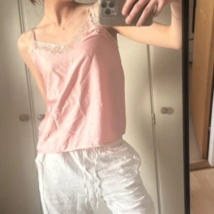 Ljusrosa linnetopp med spetsdetaljer - Säljer en söt ljusrosa linnetopp med tunna band och v-ringning. Toppen har fina spetsdetaljer längs urringningen och är gjord i ett glansigt, silkesliknande material. Perfekt för dig som gillar en romantisk och feminin stil.