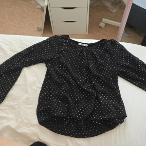 Svart prickig blus från MyHailys XS - Svart blus från MyHailys i storlek XS med vita prickar. Långärmad modell med rund halsringning och lätt, flowigt tyg som ger en snygg siluett. Perfekt att styla med jeans eller kjol för en trendig look.
