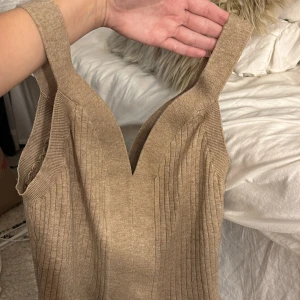 Beige ribbad linnetopp från Hailys - Supersnygg beige linnetopp från Hailys med breda axelband och v-ringning. Toppen är ribbstickad och har en figurnära passform som framhäver siluetten. Perfekt att styla med jeans eller kjol för en trendig look.