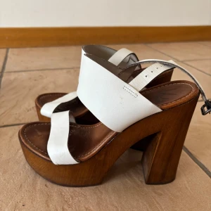 sandaler med träklack från K.Cobler - Snygga sandaler från K.Cobler med breda vita remmar i skinn och träklack. 