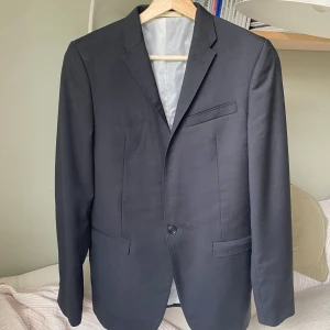 Svart kavaj från Acne Studios 48/S - Stilren svart kavaj från Acne Studios i klassisk modell med smal krage och tre fickor framtill. Fodrad insida i ljus färg och enkelknäppning med en knapp. Perfekt för dig som vill ha en clean och tidlös look. Köpt för 8 tusen drygt 