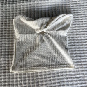 Vit bandeau tubtopp i bomull - Säljer en vit bandeau tubtopp med snygg twistad detalj framtill. Toppen har en strukturerad, våfflad yta som ger en cool känsla och är tillverkad i mjuk bomull. Perfekt för varma dagar eller lager på lager-stil.
