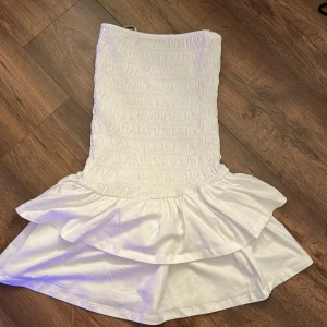 Vit volangklänning från Gina Tricot - Supersöt vit kortklänning från Gina Tricot med smockad överdel och tunna axelband. Klänningen har dubbla volanger nertill som ger en riktigt somrig vibe. Perfekt för midsommar. Möts gärna upp i Stockholm!