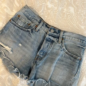 Blå jeansshorts från Levi's - Säljer ett par klassiska blå jeansshorts från Levi's, modell 501. De har en snygg slitning och fransiga kanter, bra skick!!