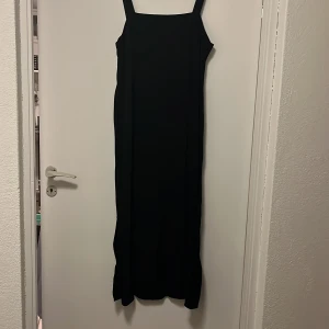 Svart långklänning från Marianne James - Elegant svart långklänning från Marianne James med breda axelband. Perfekt för en stilren look. Klänningen har en klassisk design som passar till många tillfällen.