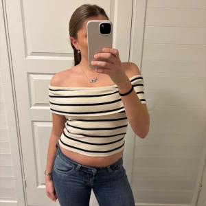 Randig offshoulder topp - Säljer en stilren offshoulder topp med svarta ränder på vit bakgrund. Toppen är super fin och knappt använd 