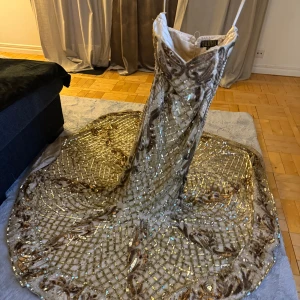 Glittrig långklänning med paljetter - Säljer en fantastisk glittrig långklänning med ett intrikat mönster av paljetter och broderier. Klänningen har en elegant passform och en vacker släp. Perfekt för en glamorös kväll!