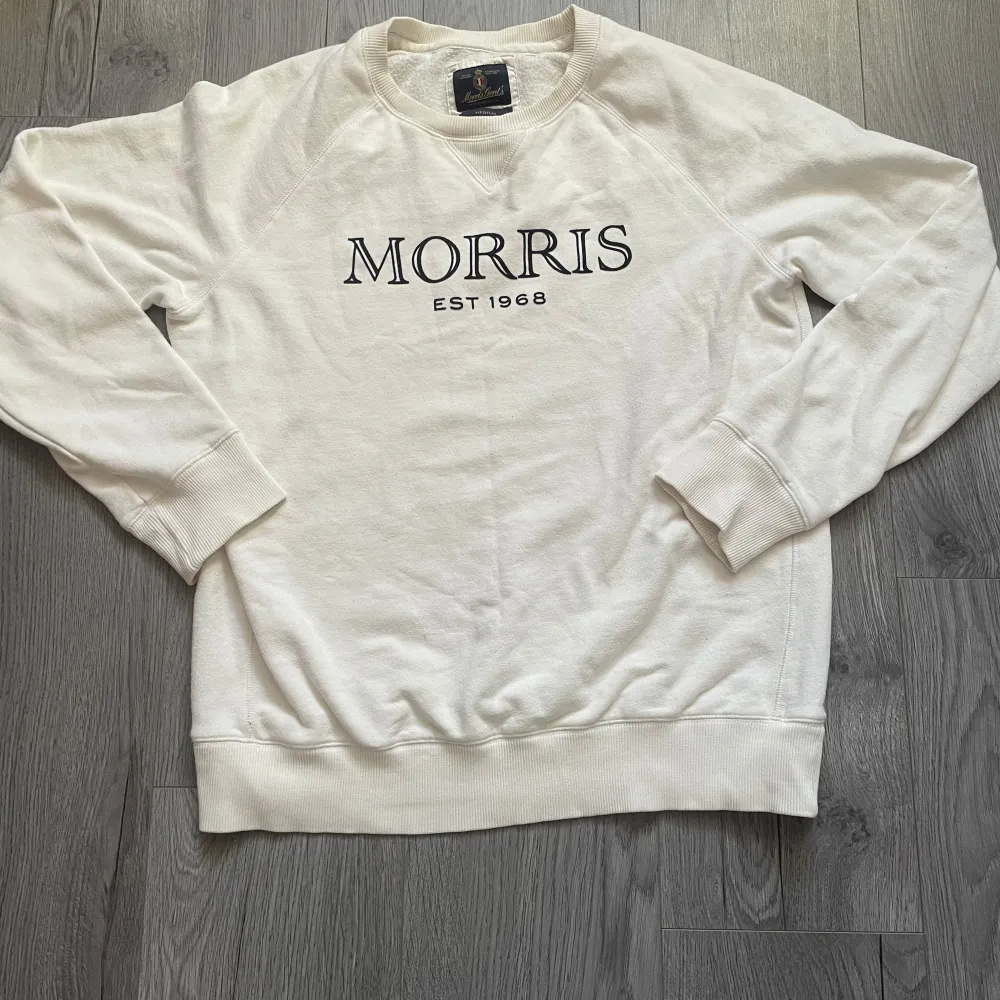 Säljer en stilren vit sweatshirt från Morris med svart text 'Morris EST 1968' på framsidan. Tröjan har långa ärmar och ribbade muddar vid ärmslut och nederkant. Perfekt för en avslappnad look. Inga defekter. Hör av er vid funderingar🤔. Hupparit & Collegepaidat.