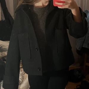 Svart kappa med knappar - Snygg svart kappa med stora fickor och knappar framtill. Jackan har en klassisk design med krage och långa ärmar.  Den är stilren och lätt att matcha med olika outfits. Pris kan diskuteras. Säljer en likadan i brunt!
