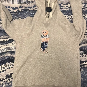 Grå hoodie från Ralph Lauren - Säljer en snygg grå hoodie från Ralph Lauren med den ikoniska Polo Bear på framsidan. Säljer den för att den är för kort på mig och den är i storlek L men den är mer som en M. Den är helt ny. Pris kan diskuteras vid snabbt affär. 