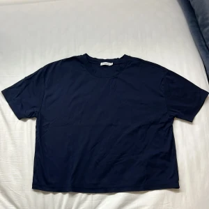 Mörkblå t-shirt från Stockh LM - Säljer en stilren mörkblå t-shirt från Stockh LM i storlek XS. T-shirten är tillverkad av 100% bomull och har en klassisk rund halsringning. Perfekt för en avslappnad look.