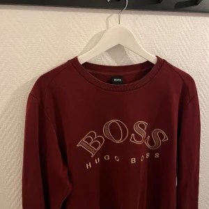 Vinröd sweatshirt från Hugo Boss - Snygg vinröd sweatshirt från Hugo Boss med broderad logga på framsidan. Tröjan har långa ärmar och ribbade muddar vid ärmslut och nederkant. Perfekt för en stilren och avslappnad look. Storlek L ✅ passar M✅ Pris 320kr ✅✅