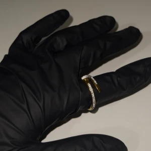 Guldfärgad ring med stenar - Elegant guldfärgad ring med en unik design som liknar en böjd spik. Helt oanvänd, köpt utomlands. Materialet är rostfritt stål med 18K guldplätering. 