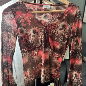 Blommig långärmad topp - Säljer en färgglad blommig topp i storlek S. Toppen har långa ärmar och ett vackert mönster i rosa, brunt och beige. Perfekt för att liva upp garderoben med lite färg och stil.