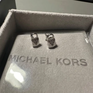Silverörhängen från Michael Kors - Silverörhängen från Michael Kors i form av små hänglås med glittrande detaljer. Kommer i originalförpackning✨