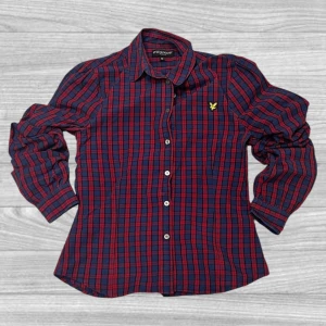 Rutig skjorta från Lyle & Scott - Säljer en snygg rutig skjorta från Lyle & Scott i rött och blått. Skjortan har långa ärmar och knappar framtill. Perfekt för en stilren look med en klassisk krage och det ikoniska Lyle & Scott-emblemet på bröstet.