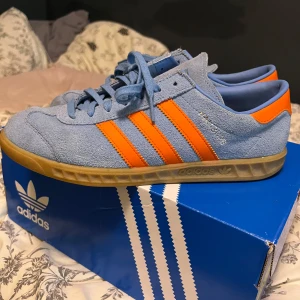 Adidas Hamburg i blå och orange - Snygga Adidas Hamburg sneakers i blå färg med orangea ränder. Skorna kommer ej till användning har använt max 5 gånger därav säljer jag dom.                                                                  Priset kan diskuteras!