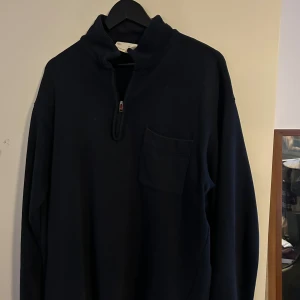 Svart långärmad tröja med dragkedja - Säljer en stilren svart långärmad tröja med dragkedja och hög krage. Tröjan har en praktisk bröstficka och är perfekt för kyligare dagar. Passar både till vardags och mer avslappnade tillfällen.