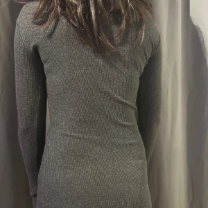 Mörkgrå ribbad klänning - Snygg mörkgrå ribbad klänning med långärmad design. Perfekt för en stilren look. Klänningen har en tight passform som framhäver figuren.