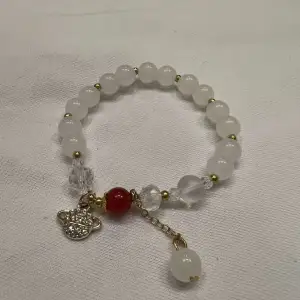 Säljer fyra unika armband med pärlor i olika färger och berlocker. Det första armbandet har vita pärlor med en röd accent och en glittrig berlock. Det andra har blågröna pärlor med en guldfärgad berlock. Det tredje armbandet är lila med en hjärtformad berlock. Det fjärde har pastellfärgade pärlor och en hjärtformad berlock.