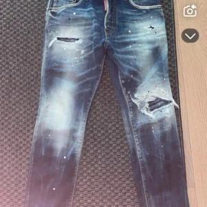 dSquared2 Jeans - Snygga blå jeans med coola slitningar och färgstänk. De har en modern look med slitna detaljer på framsidan. Perfekta för en avslappnad stil. Byxerna är äkta men tyvärr inget äktehets bevis därav lägre pris💯          Minsta lilla fundering så hör av dig!🔥