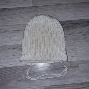 Vit stickad mössa med knytband - Säljer en mysig vit stickad mössa med ribbad design och praktiska knytband. Perfekt för kyliga dagar och håller dig varm och bekväm. Enkel och stilren design som passar till det mesta. Hemmastickad. 