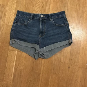 Mörkblå jeansshorts med uppvikta ben - Snygga mörkblå jeansshorts med klassisk femficksdesign och uppvikta ben. Perfekta för en avslappnad stil. De har en knapp och dragkedja framtill.