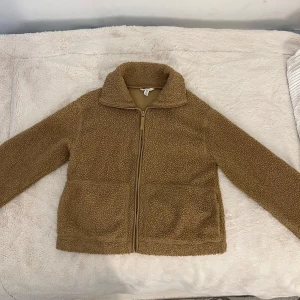 Beige teddyjacka med dragkedja - Mysig beige teddyjacka med dragkedja framtill. Jackan har en hög krage och långa ärmar, perfekt för kyliga dagar. Den har en enkel och stilren design som passar till många olika outfits. Den är i storlek M men folk som har S passar den också för. Den är som ny eftersom att den var för stor för mig och är bara använd fåtal gånger!🤎DM mig gärna om ni vill köpa.     