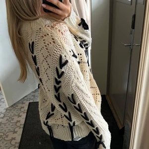 Vit stickad tröja från Medicine - Säljer en snygg vit stickad tröja från Medicine med svarta detaljer. Tröjan har ett unikt mönster med svarta snörningar längs ärmarna och sidorna. Säljer då den inte kommer till användning. Skicka gärna prisförslag. 