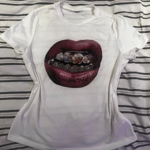 Vit t-shirt med konsttryck - Säljer en vit t-shirt med ett unikt tryck av läppar och konstverk i mitten. T-shirten har korta ärmar och en normal passform. Perfekt för dig som vill ha något annorlunda i garderoben!
