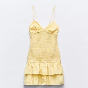 Gul rutig klänning med volang - Söt gul rutig klänning med smala axelband och volangdetalj. Perfekt för sommarens varma dagar. Den har en smickrande passform med en liten rosett framtill. Ny med prislapp