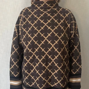 Polotröja i brunt och beige från Malene Birger - Säljer en snygg polotröja med brunt och beiget mönster. Tröjan har långa ärmar och en hög krage. Storlek L. Mycket fint skick.