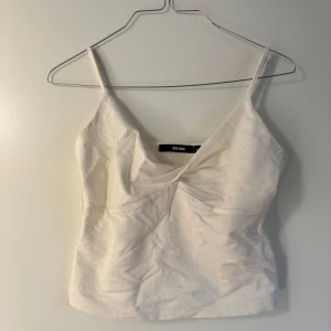 Vit linnetopp  - Säljer en stilren vit topp från Bik Bok i linnematerial. Toppen har smala axelband och en omlott-design framtill som ger en snygg detalj. Perfekt som ett basplagg eller till fest.