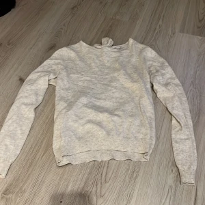 Beige tröja från ONLY - Säljer en stilren beige tröja från ONLY med långärmad design och en unik öppen ryggdetalj med knytning. Perfekt för en avslappnad men ändå chic look. Tröjan är i mjukt material och har ribbade muddar vid ärmslut och nederkant. Liten i storleken.