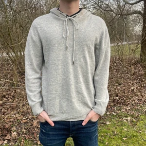 Grå Kashmir-hoodie  - Säljer en stilren grå hoodie med snörning i halsen. Tröjan har långa ärmar och en bekväm passform, perfekt för kyligare dagar. uppe vid kragen så har den gått sönder! Den är tillverkad i ett mjukt material som ger en skön känsla. Perfekt för en avslappnad look. Den är från Kina så kan inte bekräfta att det är 100 % Kashmir